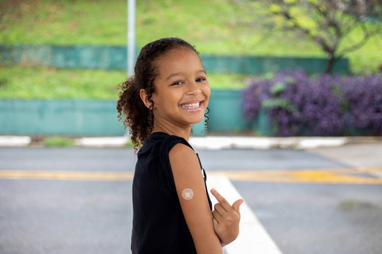 Criança aponta para braço após receber vacina