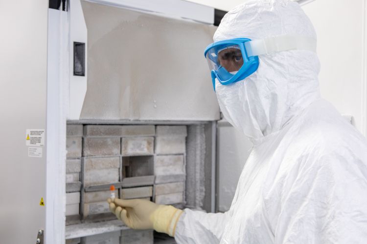 Homem paramentado segurando uma ampola com cepa vacinal em frente a um ultrafreezer