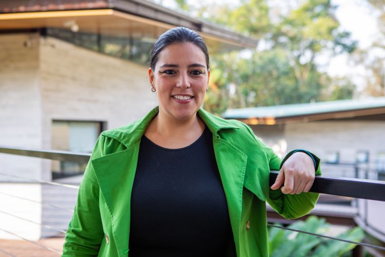 Karina Banci: mulher com cabelos morenos, camiseta preta e casaco verde em ambiente externo