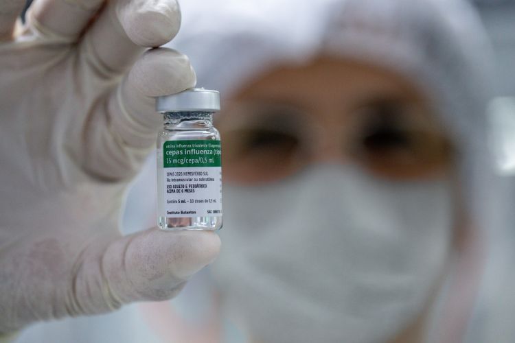 Colaborador do Instituto Butantan segurando ampola da vacina da gripe